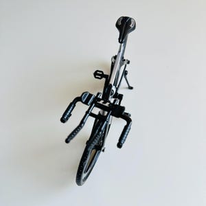 May include: A black metal toy bicycle with a silver frame and black handlebars. The bicycle has a black saddle with a white logo.