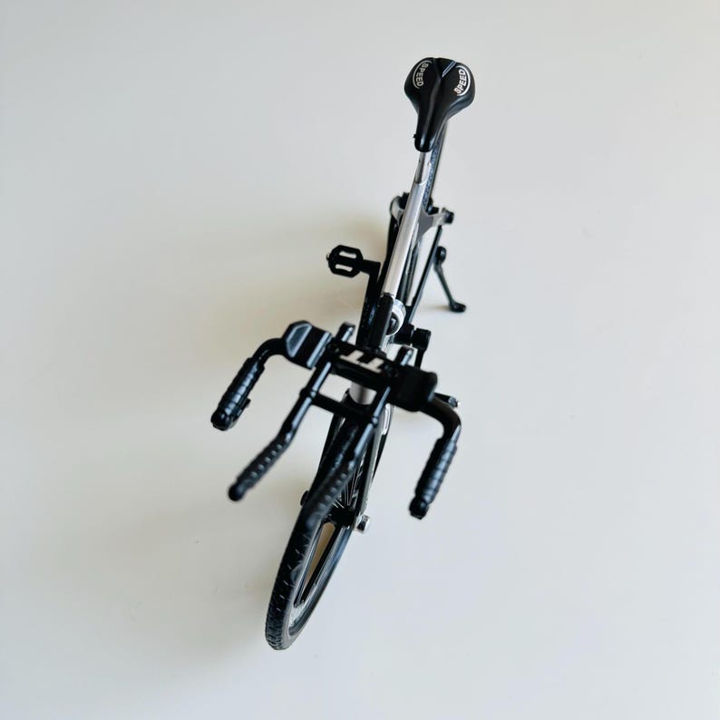 May include: A black metal toy bicycle with a silver frame and black handlebars. The bicycle has a black saddle with a white logo.