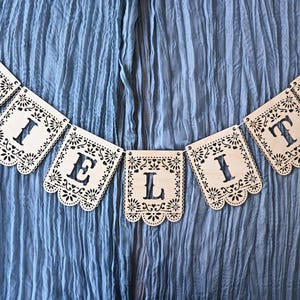 May include: A decorative banner made of eight light-colored wooden panels, each featuring intricate laser-cut floral patterns and scalloped edges. The panels are strung together to spell out the word CIELITO in bold, cut-out capital letters.