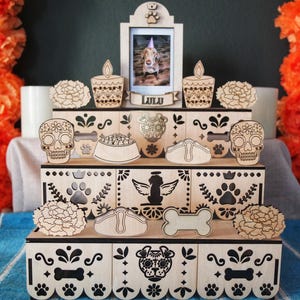 May include: A wooden pet memorial altar with a photo of a dog named Lulu. The altar features laser-cut designs of sugar skulls, dog bones, paw prints, and flowers. Orange flowers and candles flank the altar.