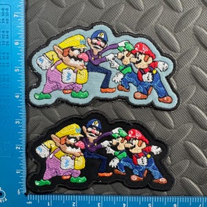 May include: Two embroidered patches featuring characters from the Super Mario video game series. The patches depict Wario, Waluigi, Mario, and Luigi in a colorful design. The patches are approximately 4 inches wide.