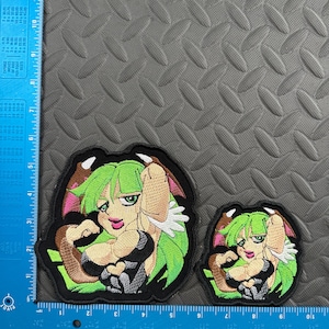May include: Two embroidered patches featuring a green-haired anime-style character with pink accents and a black outfit. The larger patch measures approximately 4 inches by 4 inches, and the smaller one is about 2.5 inches by 2.5 inches. Both are on a black background.
