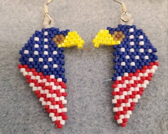 May include: A pair of beaded earrings shaped like American bald eagles with the American flag design. The earrings are red, white, and blue.