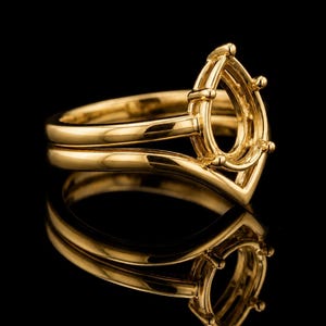 May include: A polished yellow gold ring setting featuring a pear-shaped prong mount. The band has a smooth, curved design that leads up to the central setting, which is designed to hold a single gemstone. The metal surface is highly reflective.