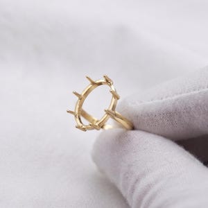 May include: A gold ring setting featuring an oval-shaped head with six prongs extending upward, designed to hold a gemstone. The band is thin and smooth, crafted from a polished yellow gold metal, showcasing a minimalist structure for jewelry assembly.