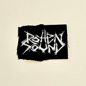 May include: Black fabric patch with white embroidered text that reads "ROTHEN SOUND".