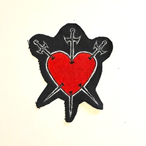 May include: A black fabric patch with a red heart pierced by three swords. The swords are silver and have cross guards.