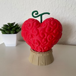 May include: A red heart-shaped fruit with a green stem, resembling a fictional fruit, on a wooden stand.