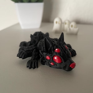 May include: A black, 3D printed spider-like creature with red eyes. The creature has a long, pointed snout and multiple legs.