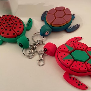 May include: Three colorful turtle keychains with segmented shells. The shells are red, green, and blue with black polka dots. The turtles are attached to silver key rings.