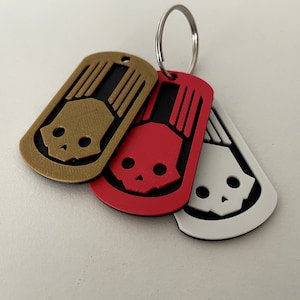 Könnte beinhalten: Drei Schlüsselanhänger aus Metall mit Totenkopf-Design. Die Schlüsselanhänger sind gold, rot und weiß.