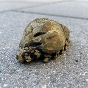 May include: A gold-colored, 3D printed figurine of a creature with a textured, segmented body and a detailed face.