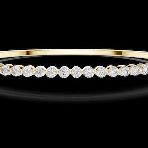 May include: A gold bangle bracelet with a row of round, clear gemstones. The bracelet is set against a black background, highlighting the sparkle of the gemstones and the shine of the gold.