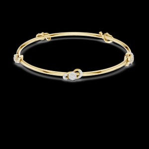May include: A gold bangle bracelet with four decorative diamond clusters. The bracelet has a simple, elegant design with a polished finish. The diamond clusters are round and add a touch of sparkle to the piece.