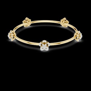 May include: A gold bangle bracelet with five floral and leaf-shaped accents. Each accent is encrusted with small, sparkling diamonds. The bracelet is set against a black background, highlighting the jewelry's design.