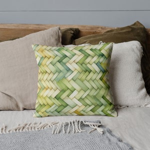 May include: A green and yellow woven pillow with a geometric pattern. The pillow is on a bed with other pillows and a blanket.