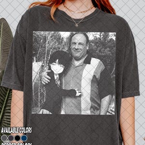 May include: Dark grey t-shirt featuring a black and white image of two people. The image is a vintage-style photograph. The text "AVAILABLE COLORS" and "PEPPER COLORS" is printed at the bottom of the shirt, along with color swatches.