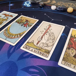 four tarot cards arranged on a blue and purple patterned surface, with various illustrations and text.