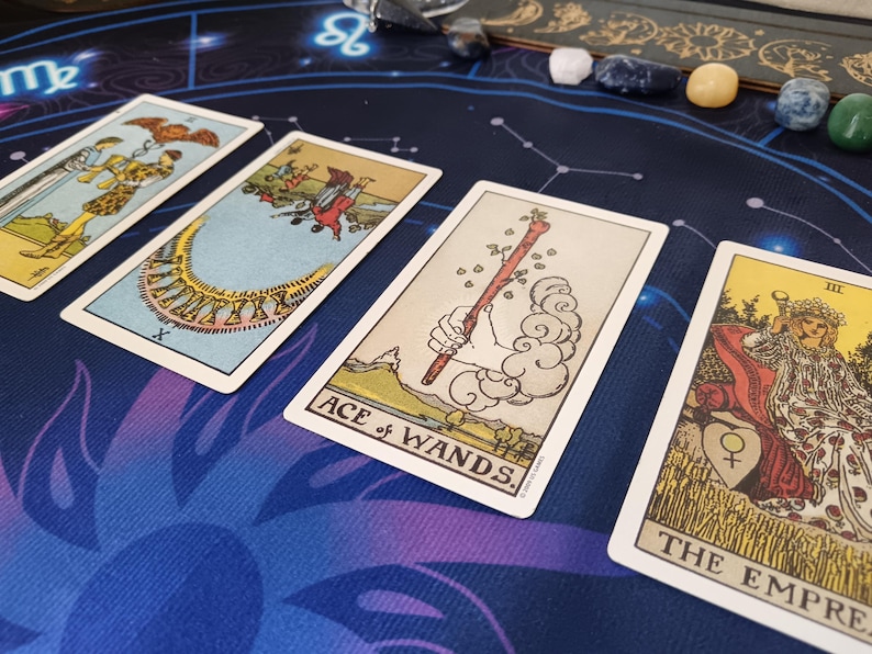 four tarot cards arranged on a blue and purple patterned surface, with various illustrations and text.