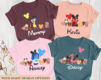May include: Four t-shirts in maroon, peach, pink, and teal, each with a cartoon character design and a name. The designs include popcorn, Mickey Mouse waffles, and coffee cups. The names are Mommy, Kevin, Ashley, and Daddy.