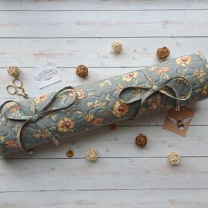 May include: A grey and yellow floral fabric roll with a ribbon tied around it. The fabric has a quilted pattern and is decorated with a small tag that says "Home Sweet Home".