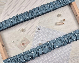 Puede incluir: Dos fundas de tela azul con patrones de corazones blancos se estiran sobre un bastidor de bordado de madera. La tela está fruncida. El fondo incluye papel estampado, pequeños cristales y una pequeña tarjeta con un diseño floral.