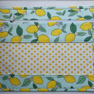 May include: A rectangular zippered pouch featuring a lemon pattern on a light blue background. The design includes yellow lemons, green leaves, and white flowers. The lower section has a quilted yellow polka dot pattern.