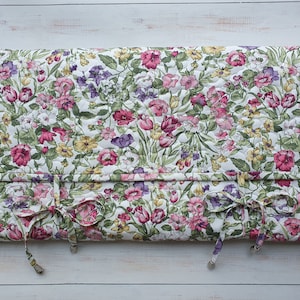 Può includere: Una trapunta a motivi floreali su sfondo bianco, con fiori rosa, viola e gialli. La trapunta è attaccata a una cornice di legno con lacci. Il design è in stile classico e vintage.