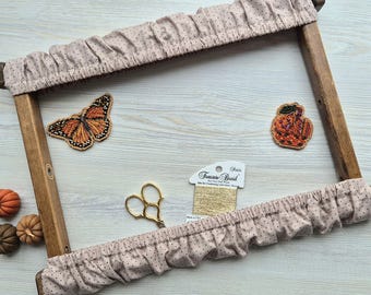 May include: A wooden embroidery hoop with a dotted fabric cover, alongside a beaded butterfly and pumpkin-shaped embellishments. Gold scissors and thread are also present, suggesting a crafting theme.