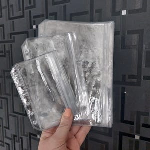 Könnte beinhalten: Drei durchsichtige Kunststofftaschen mit Reißverschluss in verschiedenen Größen, jede mit einem verstärkten Seitenstreifen mit sechs gestanzten Löchern zum Einheften in einen Ordner. Die Taschen sind transparent und haben einen Reißverschluss.