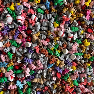Puede incluir: Una densa colección de figuritas en miniatura de colores. El surtido incluye varias formas y personajes, como patos, muñecos de nieve y formas abstractas, en tonos rosa, verde, amarillo y gris. Las figuritas parecen estar hechas de un material blando.