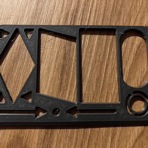 Könnte beinhalten: Ein schwarzes, rechteckiges Multi-Tool mit verschiedenen Aussparungen. Das Werkzeug hat eine Raute, ein Rechteck, einen Kreis und andere geometrische Designs. Das Werkzeug besteht aus einem soliden, mattschwarzen Material.