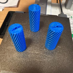 May include: Three blue 3D printed cylindrical objects with a textured surface. The objects are arranged in a triangular pattern on a black surface.
