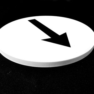 May include: A white round sign with a black arrow pointing down.