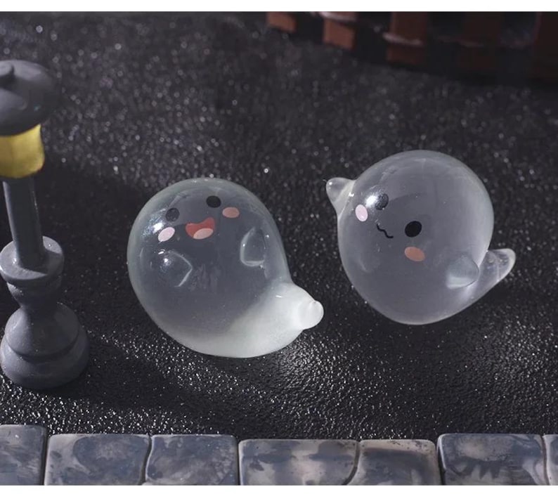 Pode incluir: Duas figuras de fantasmas cinzentos transl&uacute;cidos com bochechas rosadas e tra&ccedil;os faciais pretos. Um fantasma tem um sorriso de boca aberta, o outro um sorriso de boca fechada. Os fantasmas est&atilde;o numa superf&iacute;cie escura.