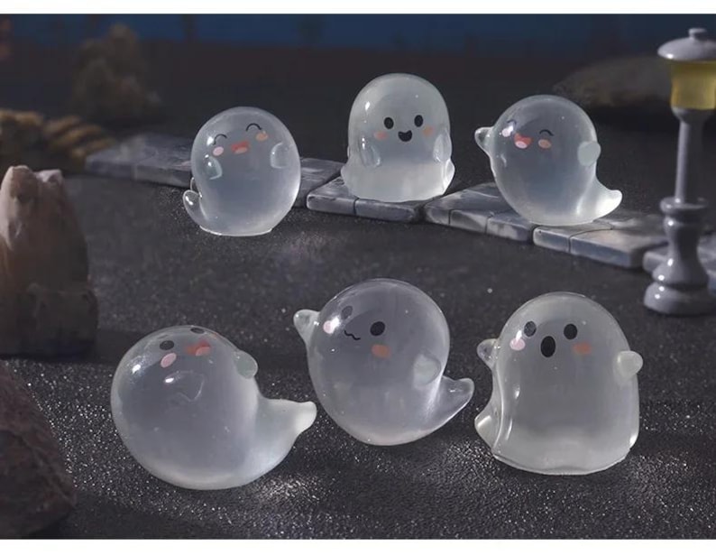 Pode incluir: Seis figuras transl&uacute;cidas de fantasmas com rostos sorridentes e bochechas rosadas. Os fantasmas t&ecirc;m bra&ccedil;os pequenos e uma parte inferior fluida. Est&atilde;o dispostos sobre uma superf&iacute;cie escura, sugerindo um tema de Halloween ou assustador.