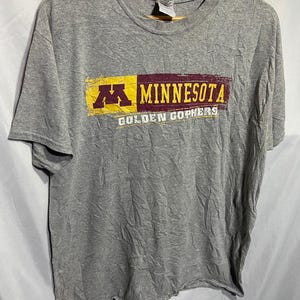 Puede incluir: Camiseta gris con un gráfico desgastado del logotipo de la Universidad de Minnesota y las palabras "Minnesota Golden Gophers".
