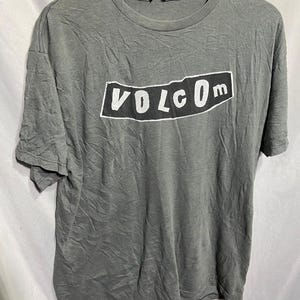 May include: A gray t-shirt with a black rectangle and the word "VOLCOM" in white letters.