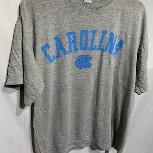 Puede incluir: Camiseta gris con un dise&ntilde;o de arco azul "CAROLINA" y un logotipo azul "UNC".