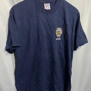 Puede incluir: Una camiseta azul marino con un logotipo de la NYPD bordado en la parte delantera. El logotipo es un escudo con una estrella y las palabras "Police Department City of New York" alrededor.
