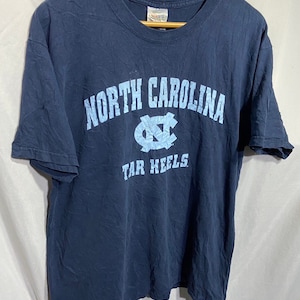 K&ouml;nnte beinhalten: Ein marineblaues T-Shirt mit einem hellblauen Aufdruck des Logos der University of North Carolina Tar Heels und dem Text "NORTH CAROLINA TAR HEELS".