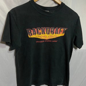 Peut inclure: T-shirt noir avec un graphisme "Backdraft" rouge et orange avec des flammes. Le texte "Universal Studios Japan" est imprimé sous le graphisme.