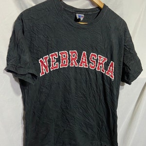Op de afbeelding: Zwart T-shirt met een geborduurd "Nebraska" logo in rood en wit.