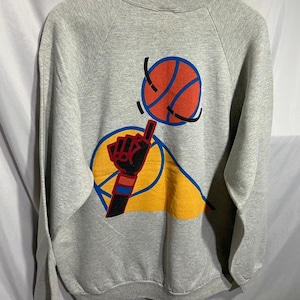 May include: A gray sweatshirt with a graphic of a basketball being passed to a hand with a finger pointing up. The graphic is in yellow, orange, red, blue, and black.