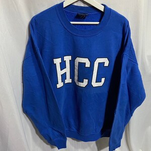 Pode incluir: Uma camisa de moletom azul royal com as letras "HCC" em branco na frente.
