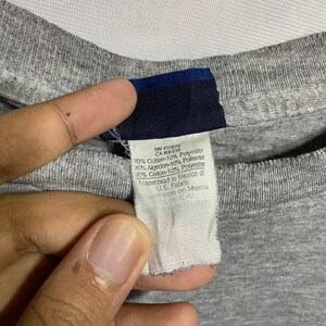 Puede incluir: Una camiseta gris con una etiqueta azul que dice "RN #90870 CA #06238 90% Algod&oacute;n-10% Poli&eacute;ster 30% Aigodon-10% Poliester 30% Algod&oacute;n-10% Poli&eacute;ster Ensamblado en M&eacute;xico de US. Tela Hecho en Mexico"