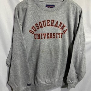 May include: Gray long-sleeve sweatshirt with the text "SUSQUEHANNA UNIVERSITY" in red embroidered on the front. The sweatshirt has a JANSport logo tag on the front.
