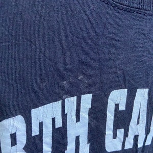 K&ouml;nnte beinhalten: Ein marineblaues T-Shirt mit wei&szlig;em Schriftzug "NORTH CAROLINA" in einer College-Schrift.