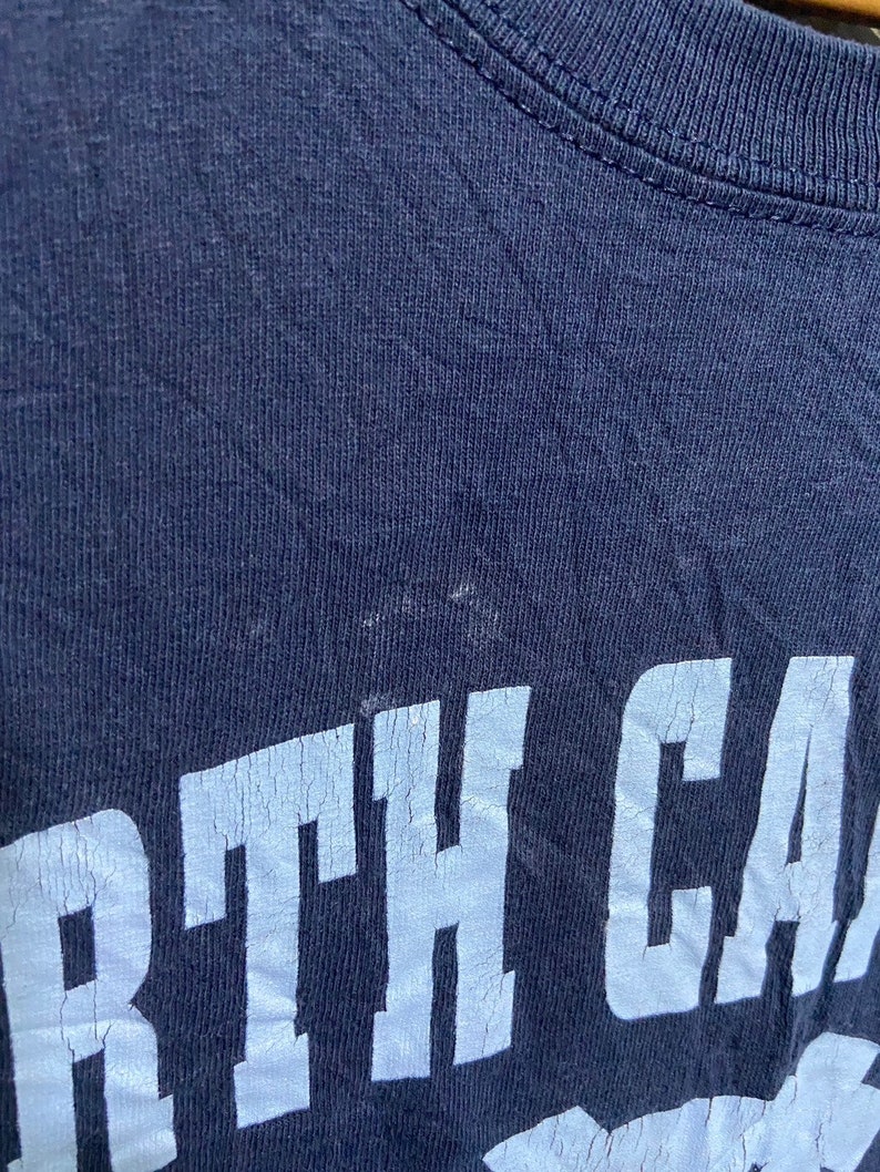 K&ouml;nnte beinhalten: Ein marineblaues T-Shirt mit wei&szlig;em Schriftzug "NORTH CAROLINA" in einer College-Schrift.