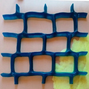 Puede incluir: Un molde de plástico azul con un patrón de cuadrícula, que se asemeja a una pared de ladrillos. El molde está parcialmente lleno de una sustancia amarilla.